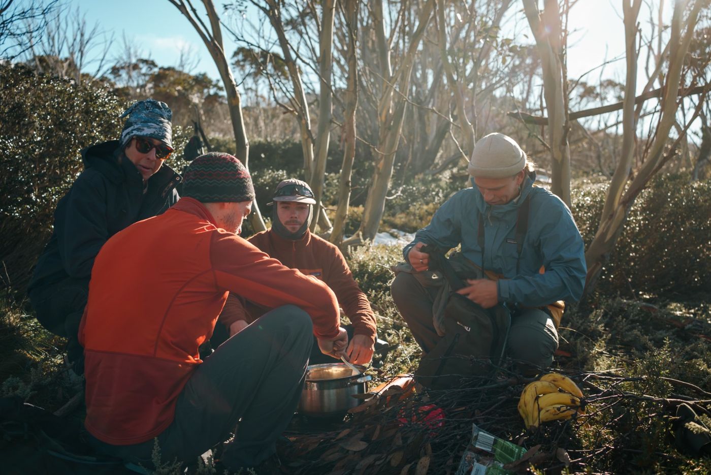 Four men eating lunch from one pot in the snow gums