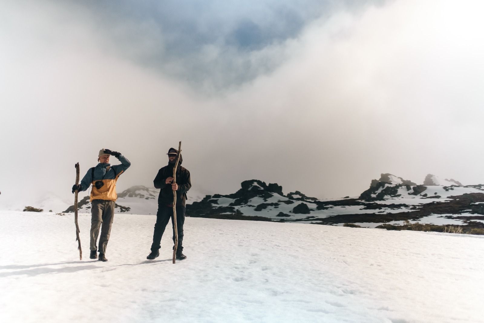 Two men with walking sticks crossing snow